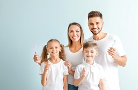 young family in white shirts holding up toothbrushes