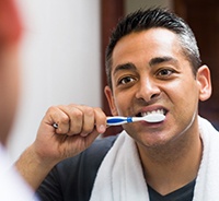 Young man looking in mirror and brushing his dental implants in Auburn