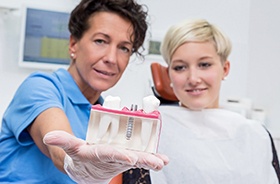 Auburn implant dentist holding dental implant model for patient