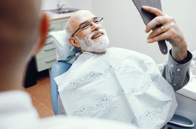 happy senior dental patient admiring new dentures in mirror