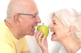 happy older couple getting ready to bite green apple