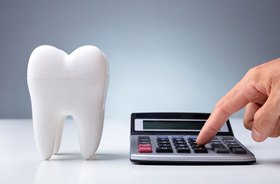 Hand using calculator next to large tooth model