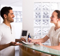 Happy patient standing at dental office front desk, paying for treatment