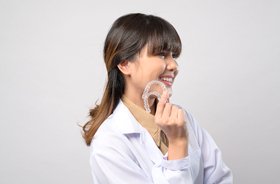 Happy Invisalign patient holding aligner and pointing at teeth
