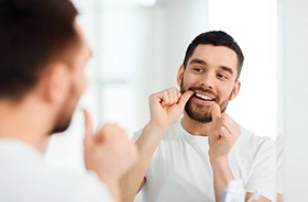 Man flossing his teeth in front of mirror