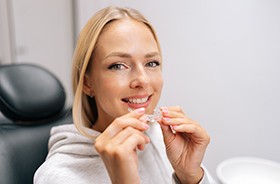 Woman in dental chair holding clear aligner
