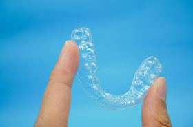 Hand holding Invisalign aligner against blue background