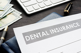 Dental insurance form next to pen, money, and computer keyboard