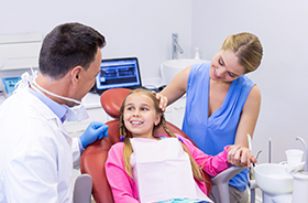 Smiling young girl in dental chair talking to dentist
