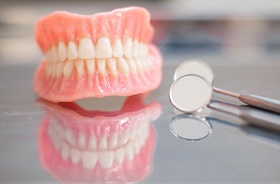 illustration of three-unit porcelain dental bridge against dark background full set of upper and lower dentures on table