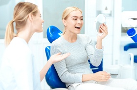 Happy dental patient using mirror to admire results of cosmetic dentistry