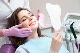 Woman using mirror to admire her smile after in-office whitening treatment