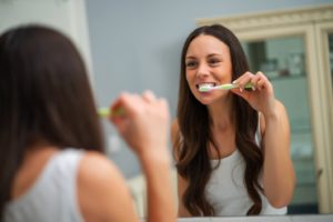 woman in white shirt brushing teeth at home