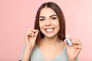 Woman flossing with Invisalign in Auburn against pink background