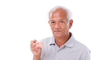 Serious older man holding full set of dentures