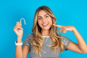 Woman holding Invisalign aligner, pointing at her teeth