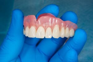 Gloved hand holding denture for upper dental arch
